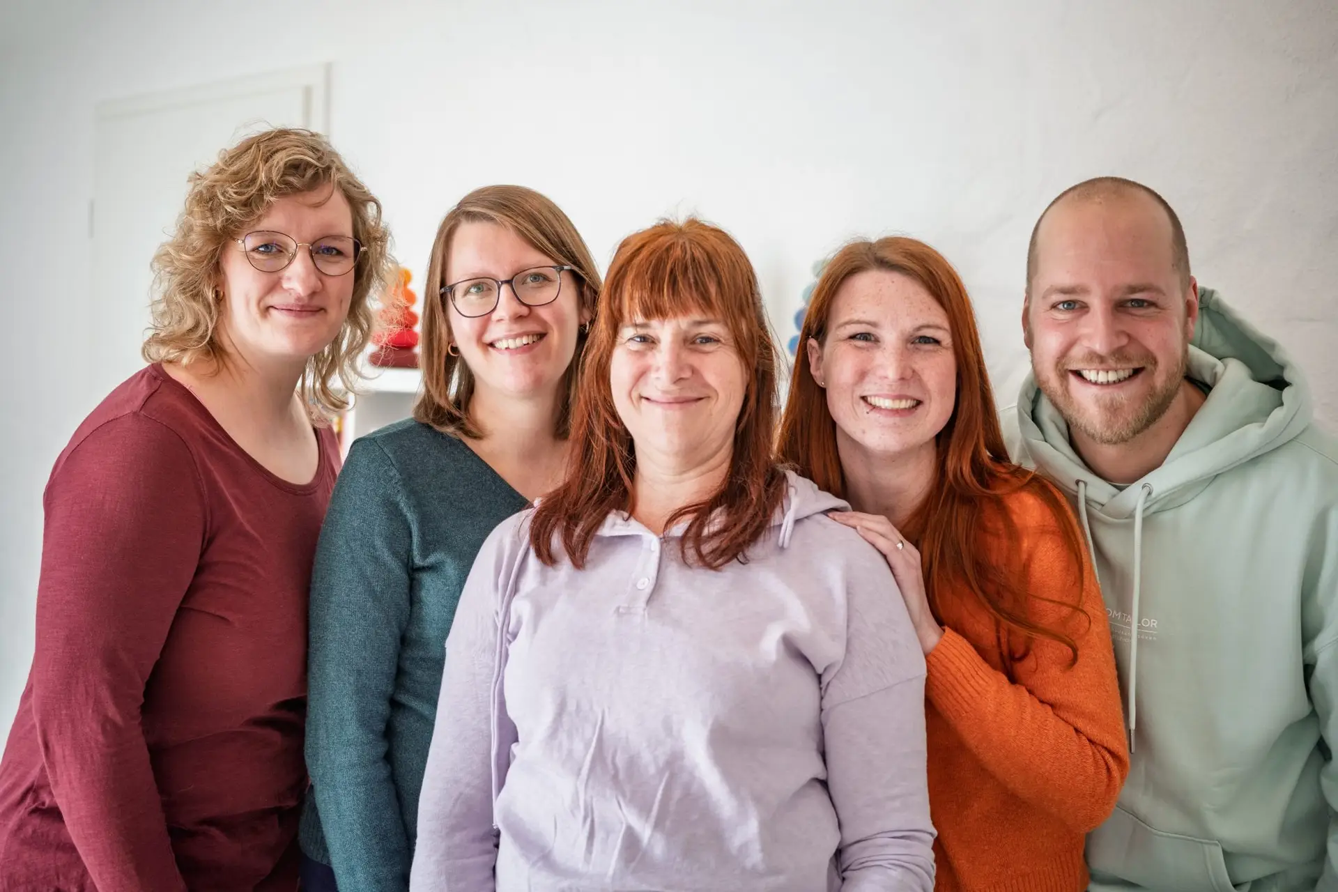 5 Logopäden stehen lächelnd eng nebeneinander. Alle tragen bunte Kleidung.