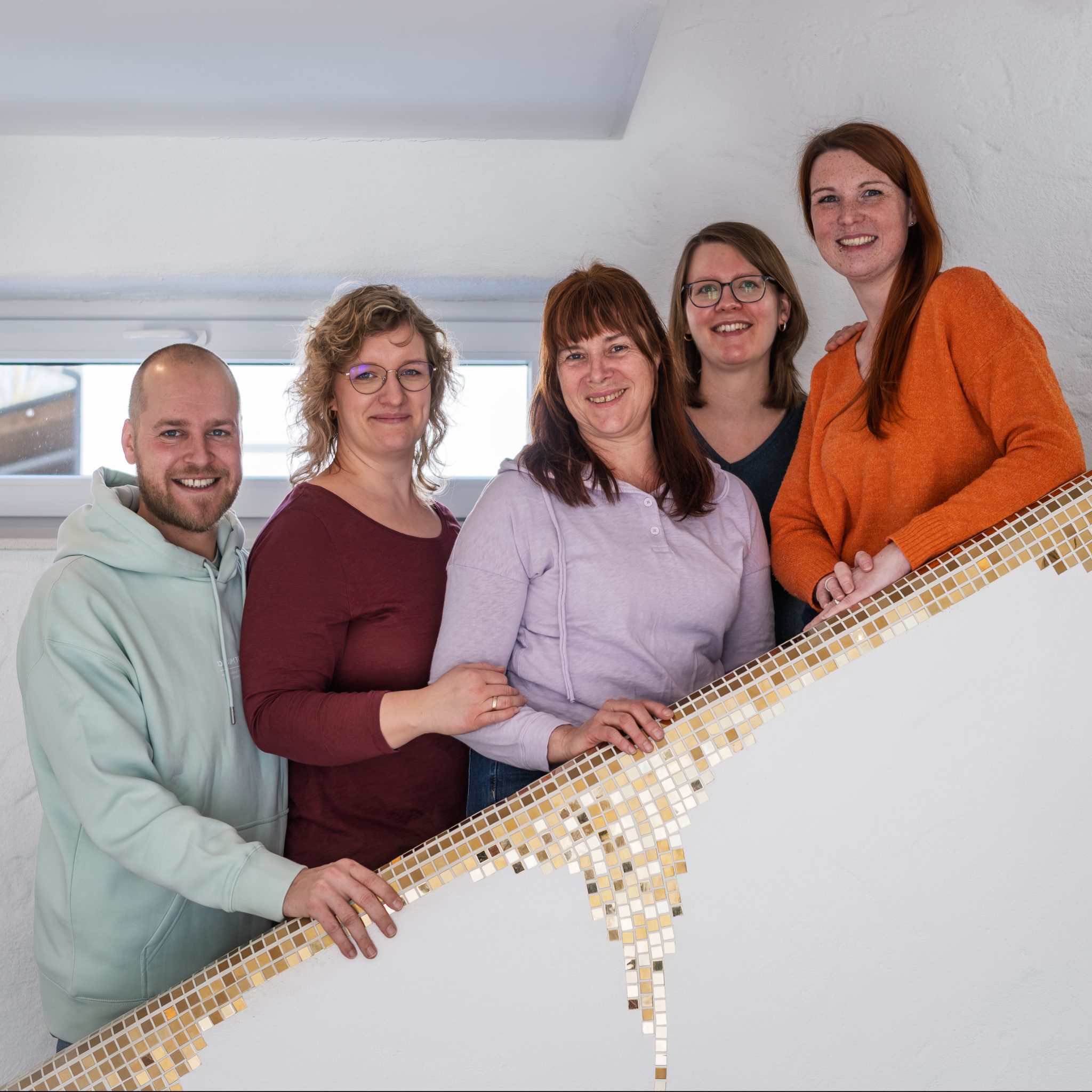 Fünf Erwachsene Menschen stehen auf einer Treppe. die abgerundete halbhohe Mauer, die das Geländer darstellt, ist mit goldenen Mosaiksteinen verziert